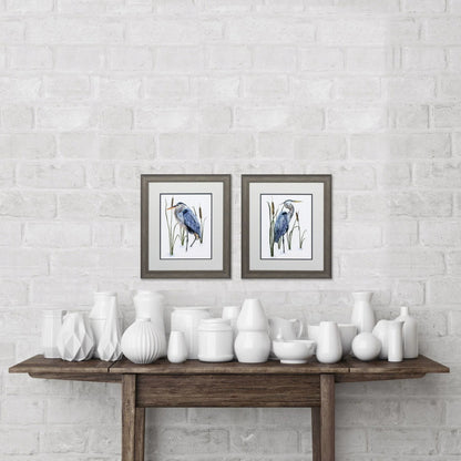 White ceramic vases on a wooden table against a white brick wall with framed artwork.